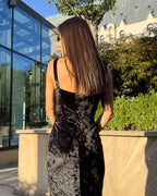 Rochie catifea neagră din catifea cu slit și bretele, purtată de model în aer liber.