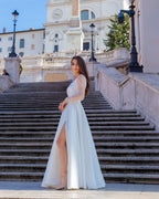 Rochie de mireasa albă lungă din satin cu șliț elegantă și decolteu frumos, fundal arhitectural.